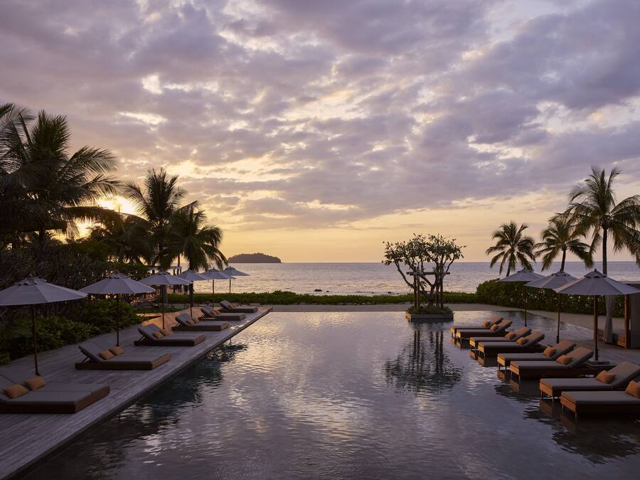 Zona de piscina con sillones y sombrillas, con vista al mar al atardecer.