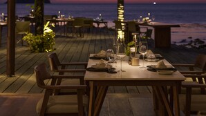 An outdoor dining area with tables set for two, overlooking a body of water at sunset. - The Retreat Koh Chang (Ko Chang)