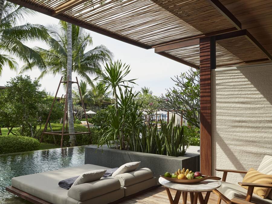 Un área de descanso junto a la piscina con terraza de madera, asientos acolchados y una mesa con fruta.