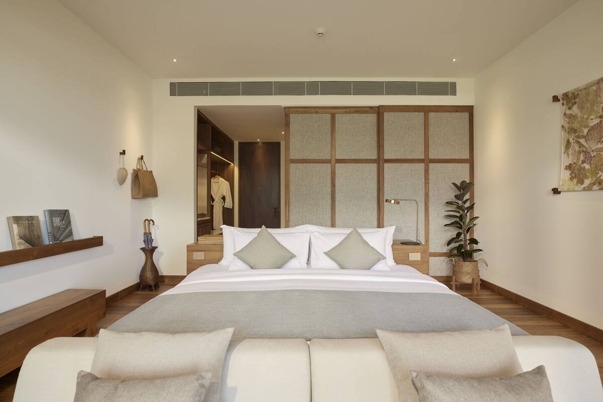 A modern bedroom with a large bed, a wooden bench, a bedside table with a vase, and a sliding door closet.