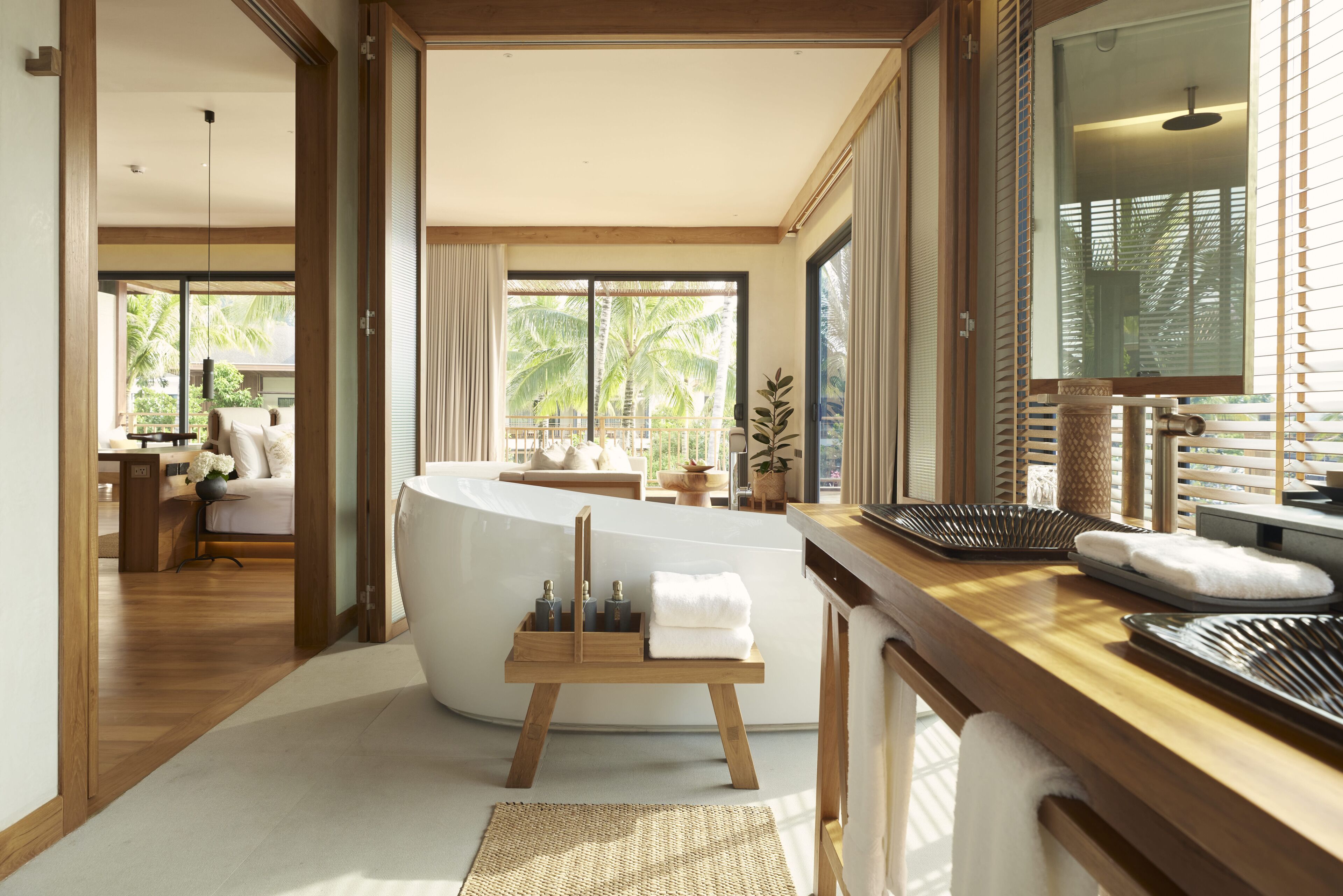 Ein modernes Badezimmer mit freistehender Badewanne, Holzelementen und Blick auf Palmen.