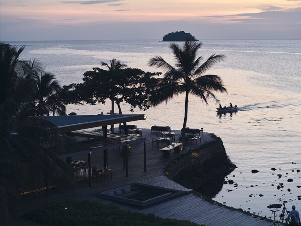 A wooden deck with outdoor seating, overlooking a calm sea with a distant island.