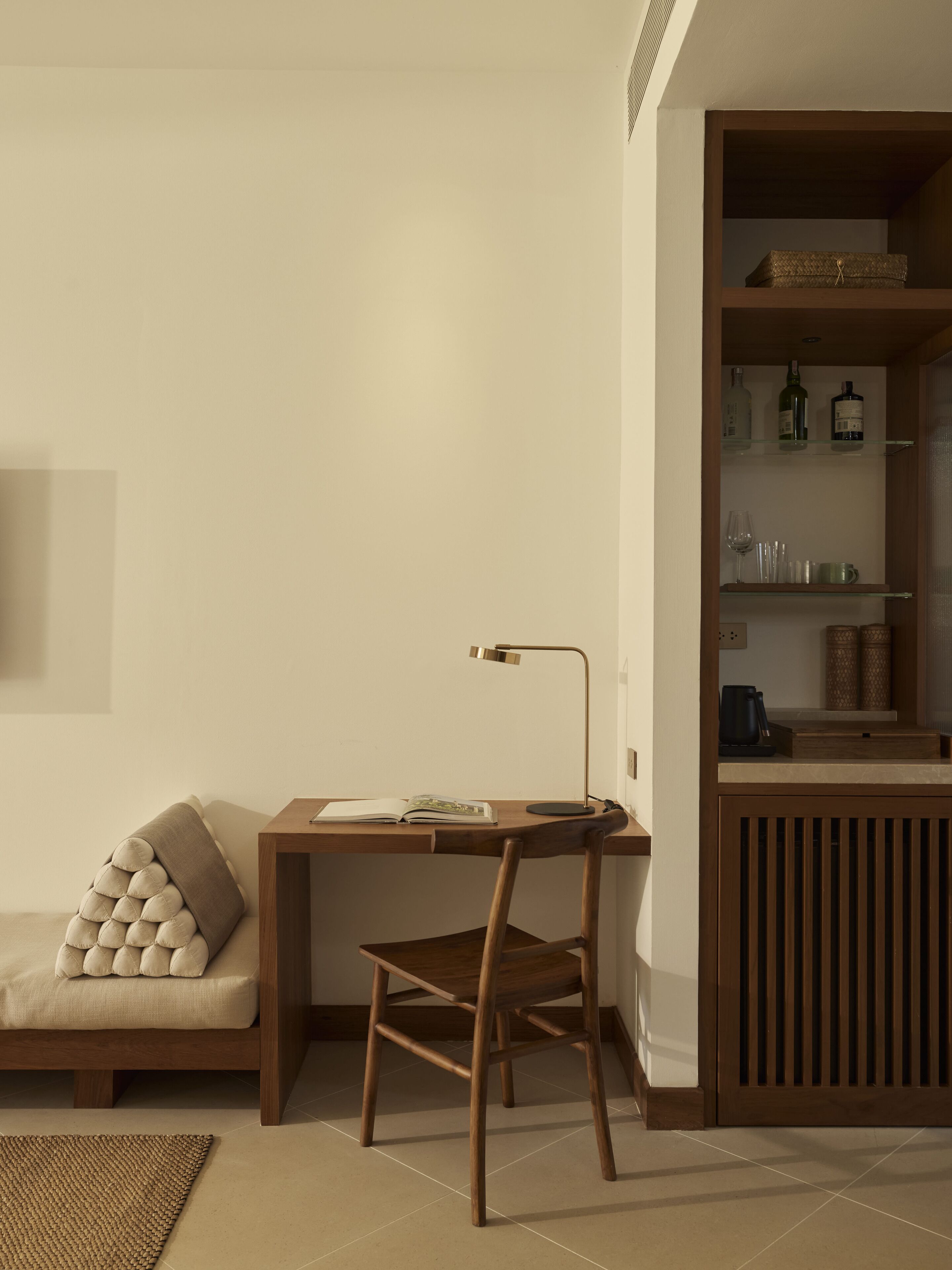 A study area with a wooden desk, a chair, and a bookshelf containing books and decorative items.