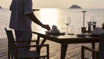 A wooden deck with a table set for two, overlooking a calm sea with a distant island.