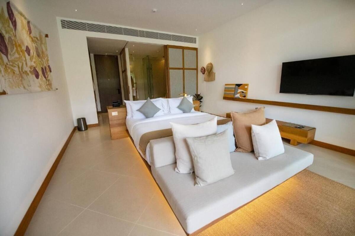 A modern hotel room with a large bed, a TV, and a view of the hallway.