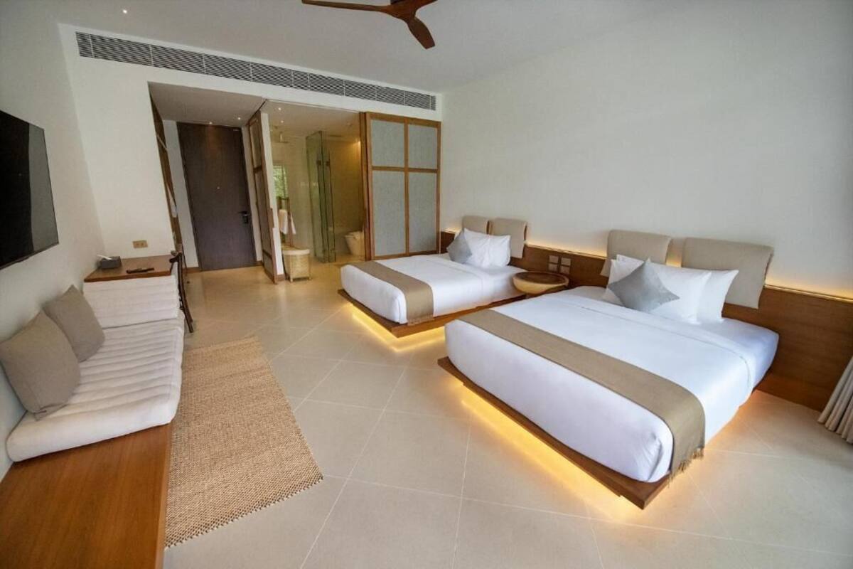 A hotel room with two beds, a sofa, a TV, and a ceiling fan.