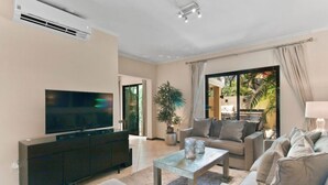 Ein modernes Wohnzimmer mit einem Flachbildfernseher, einer dunklen Unterhaltungsecke, einem Glastisch und einem beigen Sofa.
