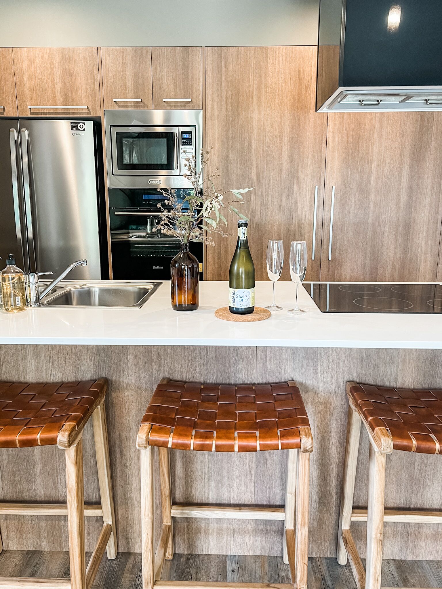 A modern kitchen with stainless steel appliances, a wooden countertop, and three woven stools.