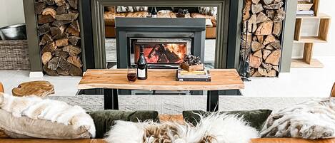 A cozy living room with a fireplace, a round mirror, and a sofa with a fluffy throw.