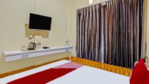 A hotel room with a bed, a TV mounted on the wall, a bedside table with a kettle, a water bottle, and a vase with flowers. - OYO 92117 Fa Homestay Syariah (Babat)