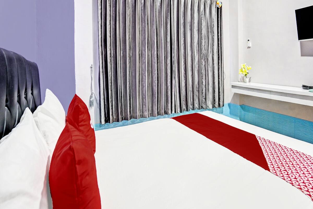 A hotel room with a bed, a TV, a desk, and a curtain.