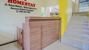 A reception desk with a wooden finish, a wall sign with contact information, and a staircase with a yellow wall. - OYO 92117 Fa Homestay Syariah (Babat)