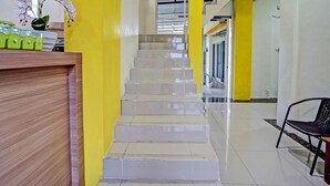 A staircase with a handrail, leading to a landing with a reception desk and a chair. - OYO 92117 Fa Homestay Syariah (Babat)