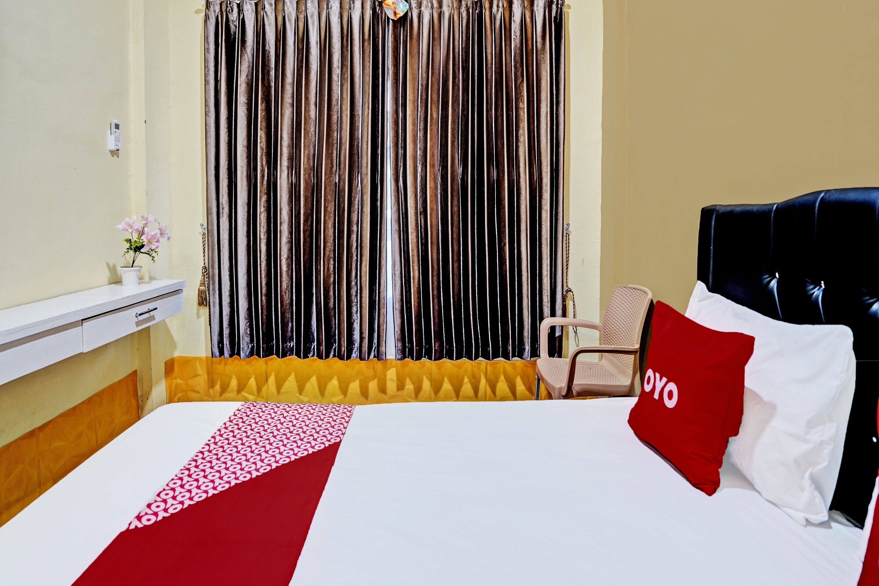 Une chambre d’hôtel avec un lit, une chaise, une petite table sur laquelle est posé un vase de fleurs, et un rideau à rayures verticales.