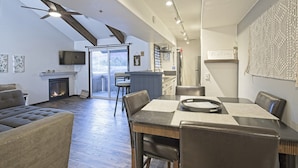 A modern living room with a fireplace, a dining area with a table and chairs, and a ceiling fan. - Park City Mountain View Condo | Amazing Ski Location! (Park City)