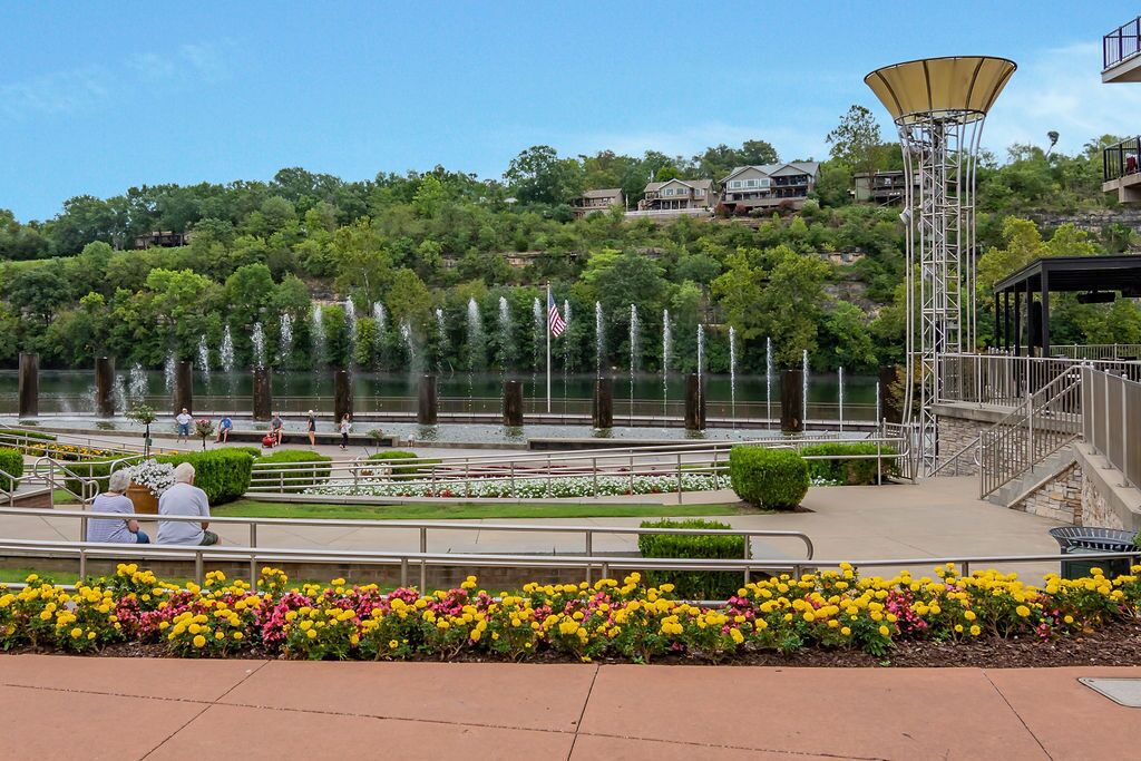 A waterfront park with a fountain, flower beds, and a gazebo.