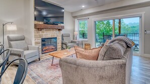 Una sala de estar moderna con chimenea de piedra, asientos cómodos y un balcón con mobiliario exterior.