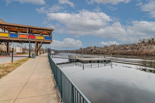 Eine Fußgängerbrücke über einem Fluss, mit einem Geschwindigkeitsbegrenzungsschild für 24 km/h, einem Betonweg und einem Metallgeländer.