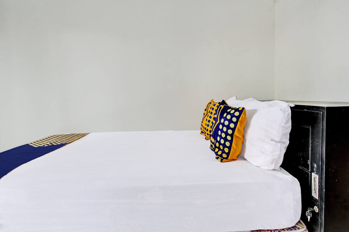 A bed with a white sheet, a blue and yellow pillow, and a black headboard.