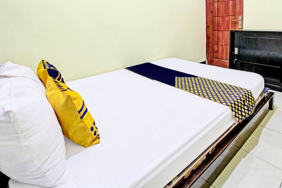 A bed with white sheets, a yellow pillow with blue patterns, and a blue and yellow checkered blanket.