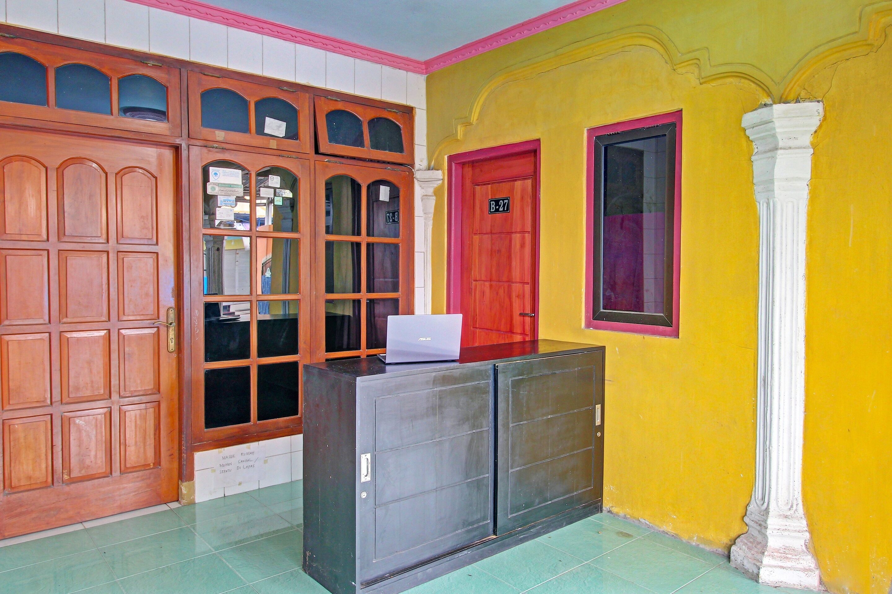A room with a wooden door marked B-27, a red door, and a window with a white column.