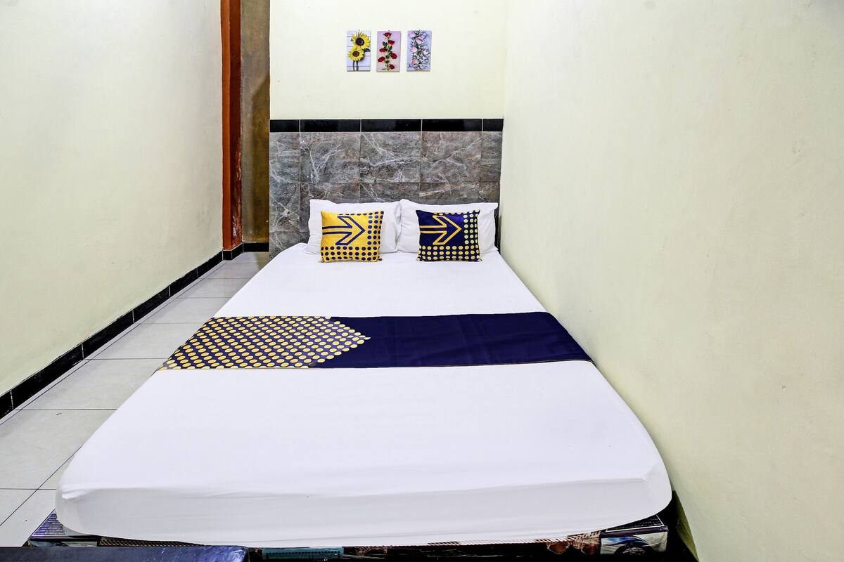A bed with a white mattress, two pillows with geometric patterns, a dark blue throw, and a marble headboard.