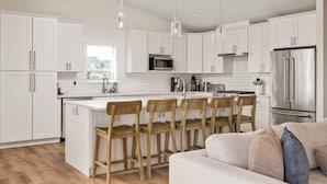 Une cuisine moderne avec des meubles blancs, un réfrigérateur en acier inoxydable et un îlot central en bois doté de tabourets de bar.