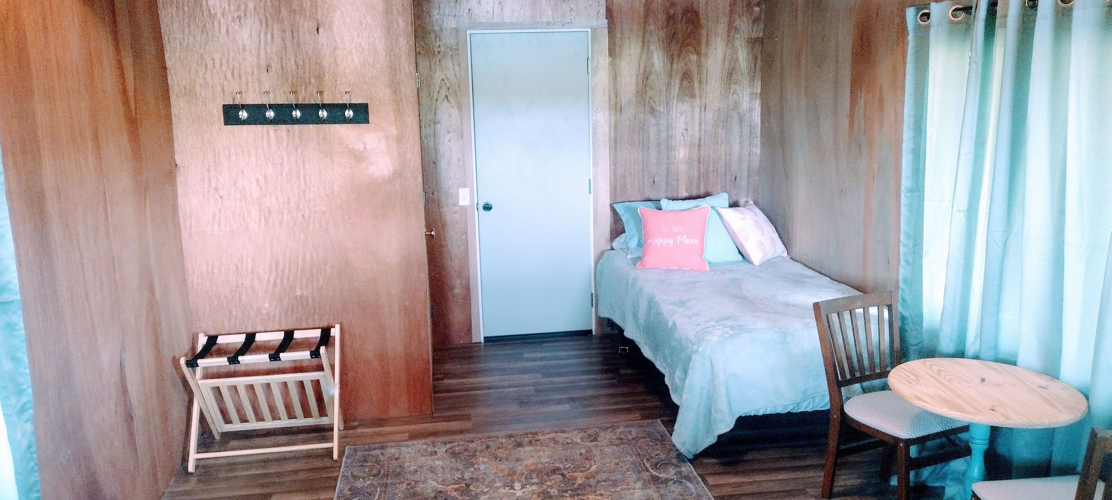 A small, cozy room with a bed, a chair, a small table, and a door.