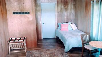 A small, cozy room with a bed, a chair, a small table, and a door.