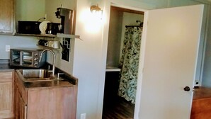 A compact kitchen with wooden cabinets, a microwave, a coffee maker, and a sink. - Minutes from Pymatuning, Cabin by the Pond (Williamsfield)