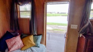 A room with a bed, pillows, and a view of a parking lot and building through an open door. - Minutes from Pymatuning, Cabin by the Pond (Williamsfield)