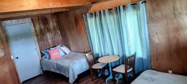 Una habitació petita i acollidora amb un llit, una cadira, una taula petita i una porta.