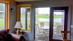 A room with a large sliding glass door leading to an outdoor seating area with a table and chairs. - Minutes from Pymatuning, Cabin by the Pond (Williamsfield)