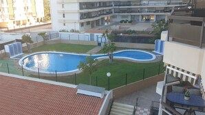 A residential area with a swimming pool, green lawns, and a multi-story building in the background. - Jardines Canarios 2 (Los Cristianos)