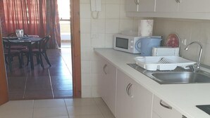 A modern kitchen with white cabinets, a microwave, a sink, and a dining area with a table and chairs. - Jardines Canarios 2 (Los Cristianos)