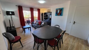 A dining area with a round table and chairs, a sofa, a TV, and a bookshelf. - Jardines Canarios 3 (Los Cristianos)