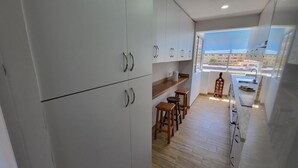 A modern kitchen with white cabinets, wooden stools, and a view of the city through large windows. - Jardines Canarios 3 (Los Cristianos)