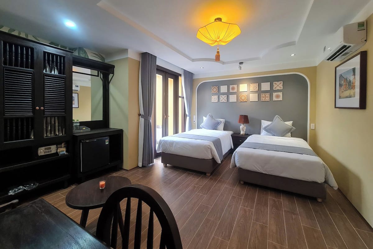 A hotel room with two beds, a desk, a chair, a wardrobe, and a ceiling light.