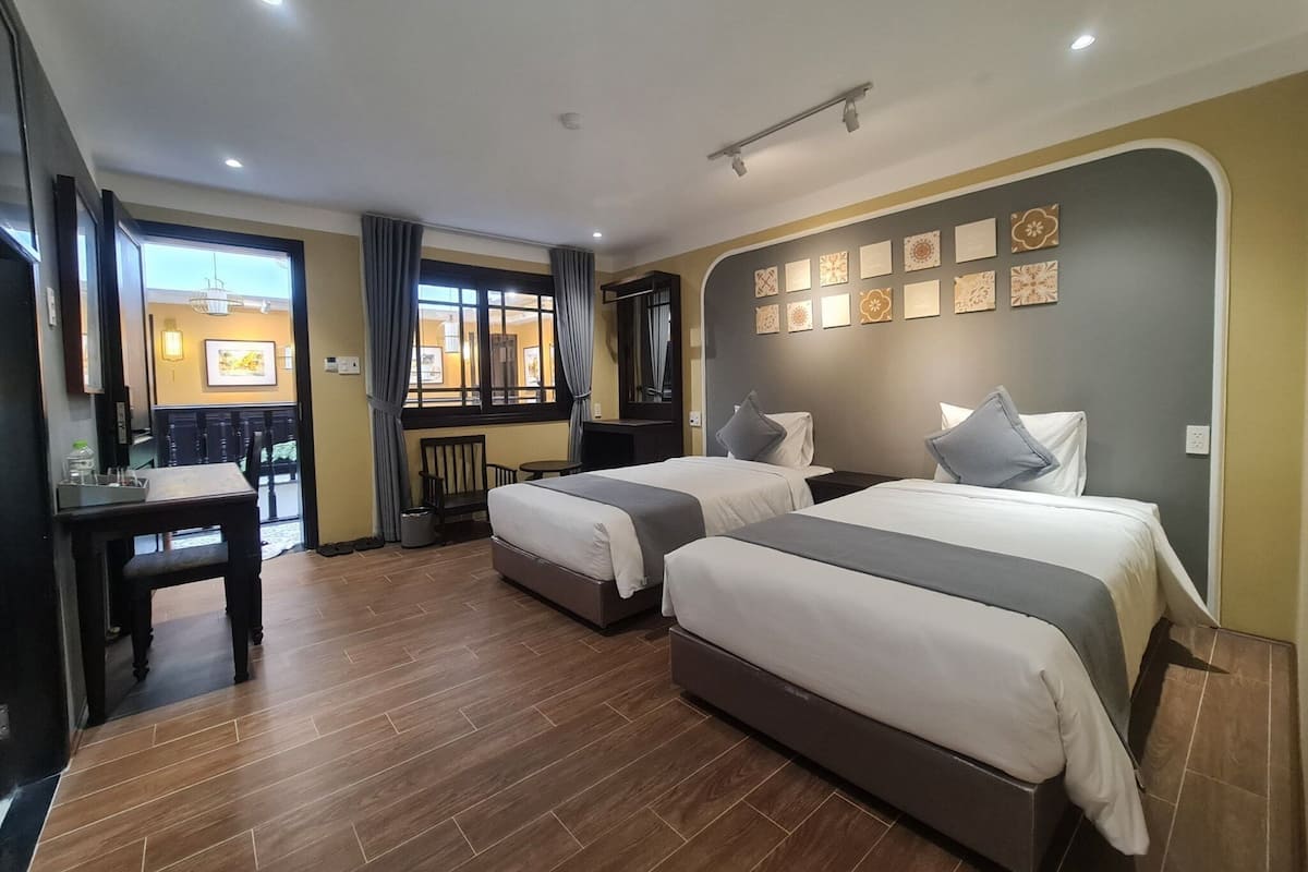 A hotel room with two beds, a desk, a chair, and a view of the dining area.