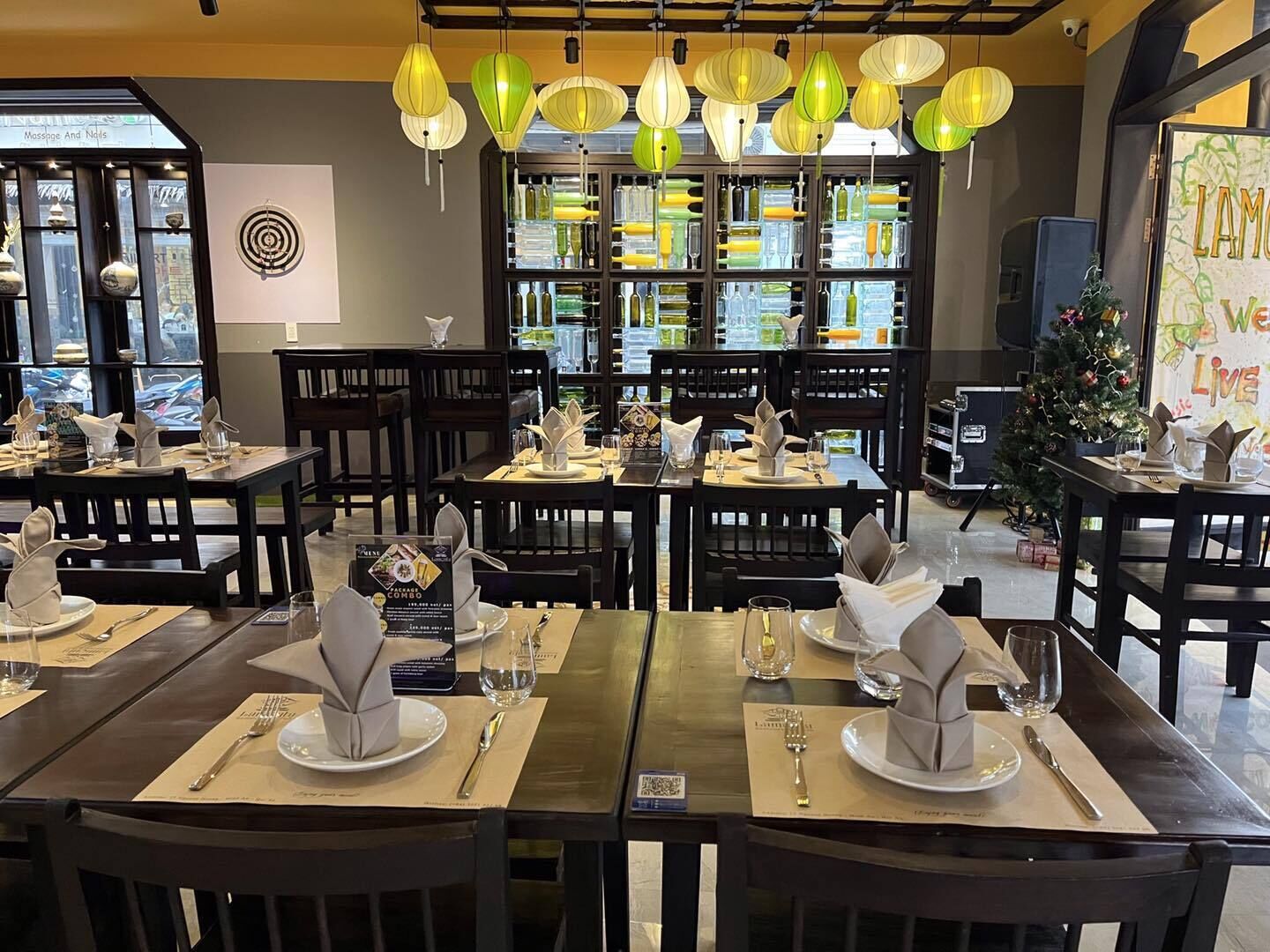 Interior de un restaurante con mesas dispuestas para comer, faroles de papel colgantes y un árbol de Navidad.
