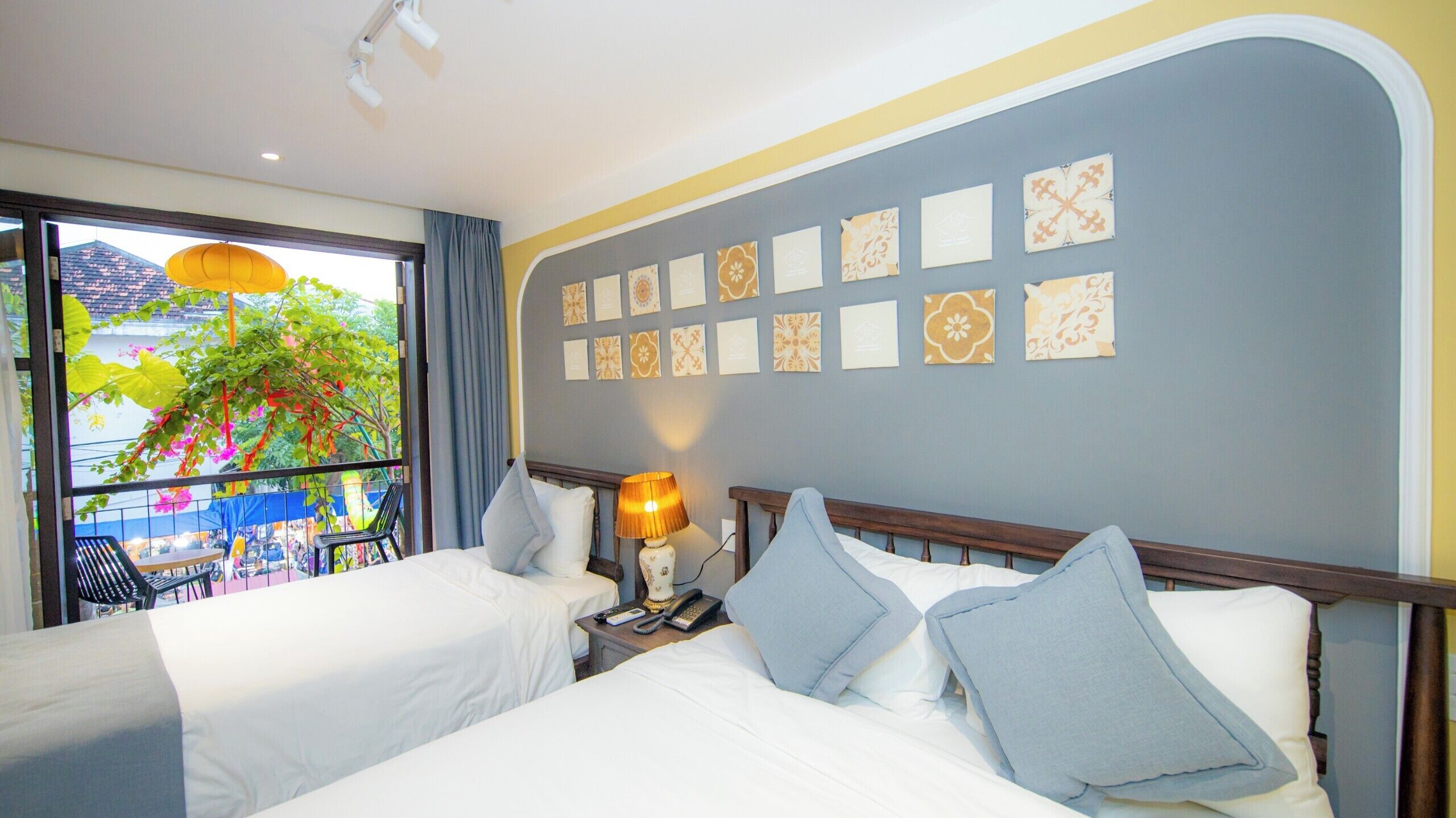 A hotel room with two beds, a balcony with a view of palm trees, and a wall decorated with patterned tiles.