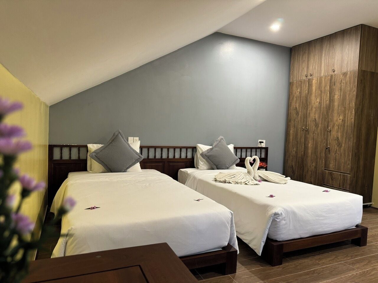 Quarto de hotel com duas camas, cabeceiras de madeira, um guarda-roupa e chão de madeira.
