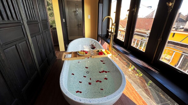 A bathroom with a freestanding bathtub, a shower, and a window with a view of buildings. - Hoianan Boutique Hotel (Da Nang)
