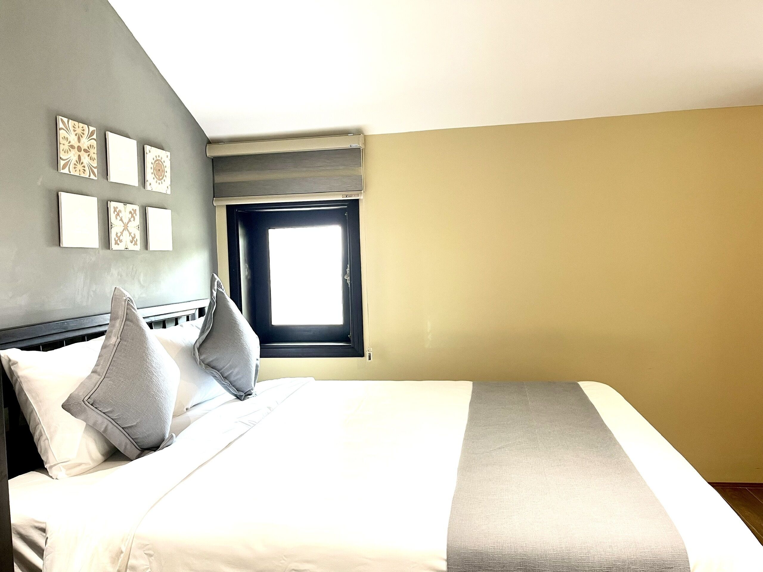 A hotel room with a bed, pillows, a window, and wall art.