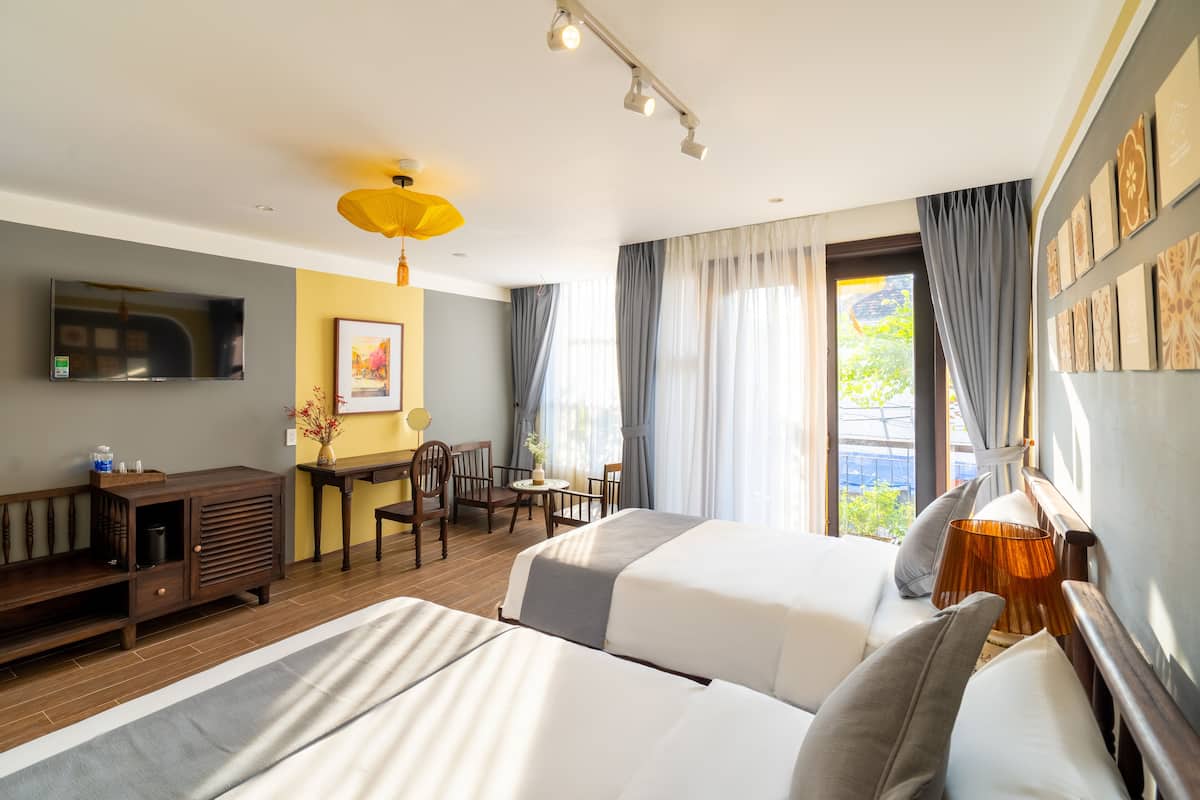 A hotel room with two beds, a desk, a chair, a TV, and a window with curtains.