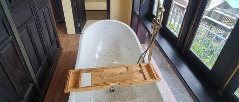 A bathroom with a freestanding bathtub, a wooden tray, and a view of the outside through large windows.