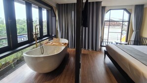 A modern bedroom with a large freestanding bathtub, a bed, and a balcony with a view of greenery. - Hoianan Boutique Hotel (Da Nang)