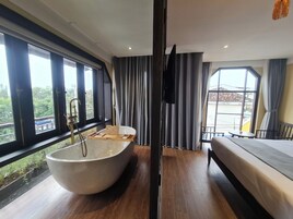 Quarto moderno com uma banheira de pé, uma cama e varanda com vista para o verde.