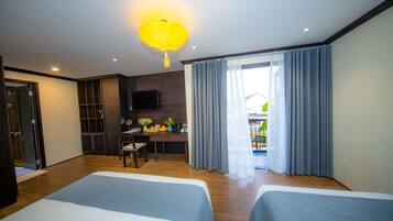 Habitación de hotel con dos camas, un escritorio con silla, televisor y ventana con cortinas.