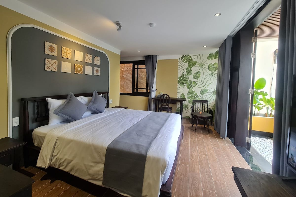 A hotel room with a large bed, a desk, two chairs, and a view of the outside.